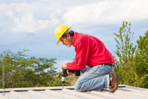 Contractor, builder installing metal panel roof with yellow hardhat