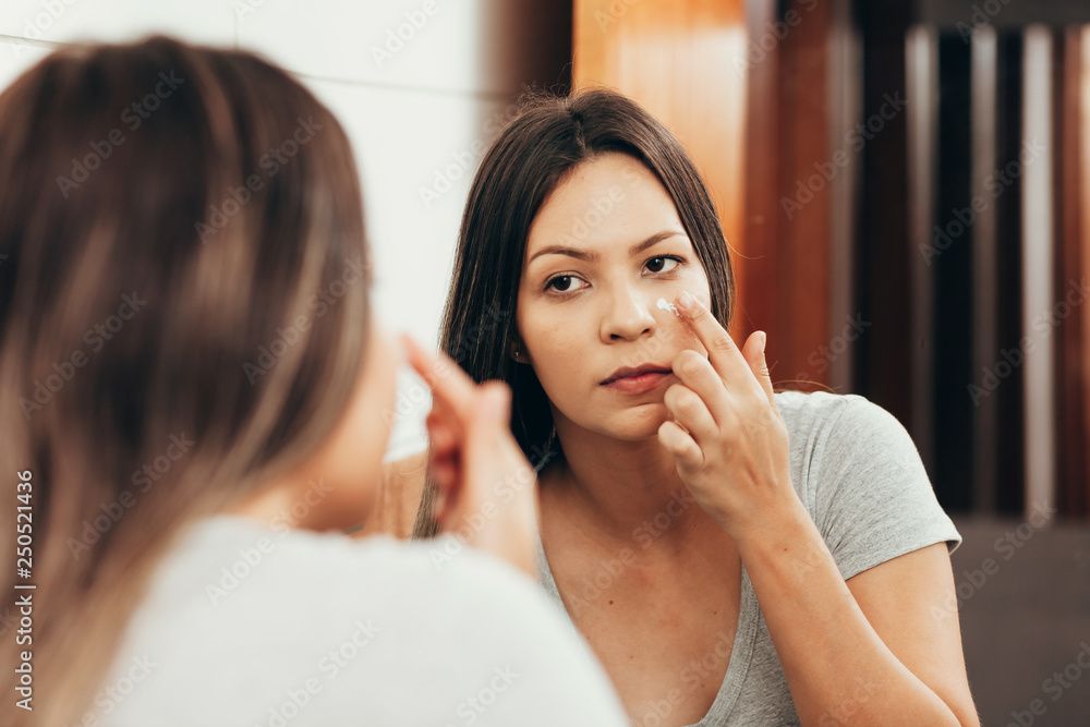 Skin care. Woman applying skin cream on her face in front of mirror Skin care. Woman applying skin cream on her face in front of mirror