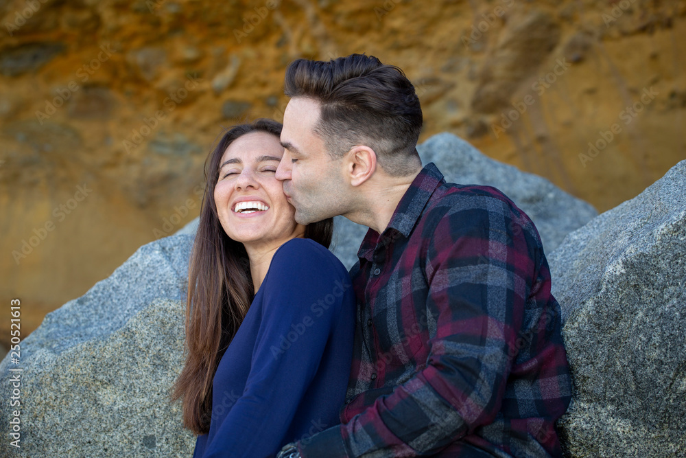 Happy Millennial Couple Sitting on Rocks Boyfriend Kissing Girlfriend Happy Millennial Couple Sitting on Rocks Boyfriend Kissing Girlfriend