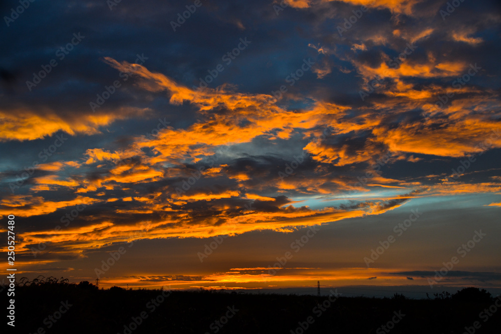 Beautiful orange clouds reflecting sunset colors above dark landscape