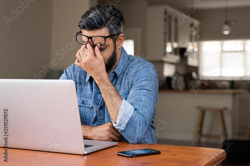 Stressed businessman with laptop computer on wooden table sitting at home photo