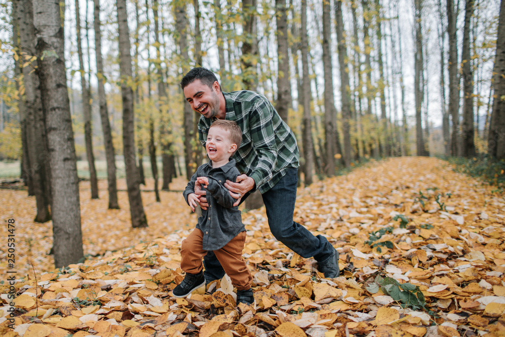 Cheerful father and son playing on dry leaves in forest during autumn Cheerful father and son playing on dry leaves in forest during autumn
