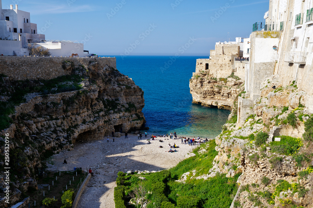 POLIGNANO A MARE, ITALY - MARCH 29th, 2018: People on lovely beach Lama Monachile with dramatic view of cliffs with caves rising from Adriatic sea in Polignano a Mare, Puglia, Italy