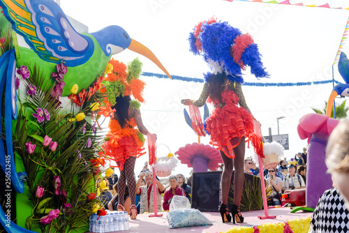 Unrecognizable group of costumed beauty design participants enjoy outdoors street show annual carnival event. Positive energy and popular recreation activities on flowers and feathers decor background