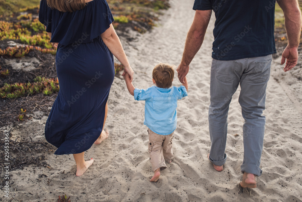 Low section of parents holding son's hands while walking on sand at beach during sunset Low section of parents holding son's hands while walking on sand at beach during sunset