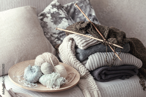 Vintage wooden knitting needles and threads for knitting on a cozy sofa with pillows and sweaters