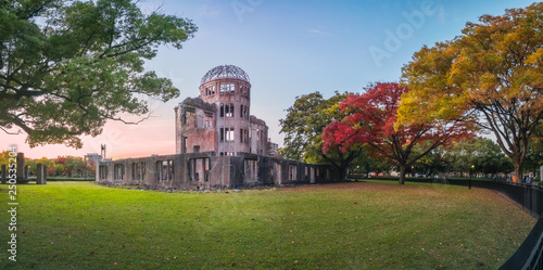 The Atomic Bomb Dome Panorama in Hiroshima and the surounding garden in autumn at sunset on the side of Motoyasu River in Japan, with the Peace Memorial Park on the left in the background.