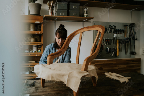 Female upholsterer upholstering wooden chair on table in workshop photo