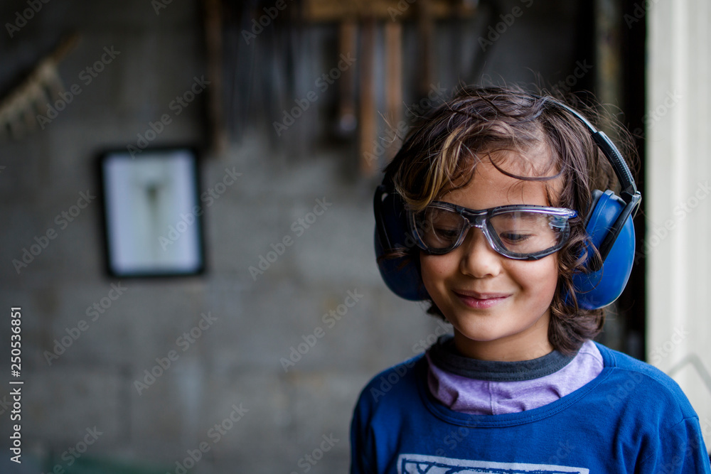 Smiling boy wearing earmuff and safety glasses standing in blacksmith