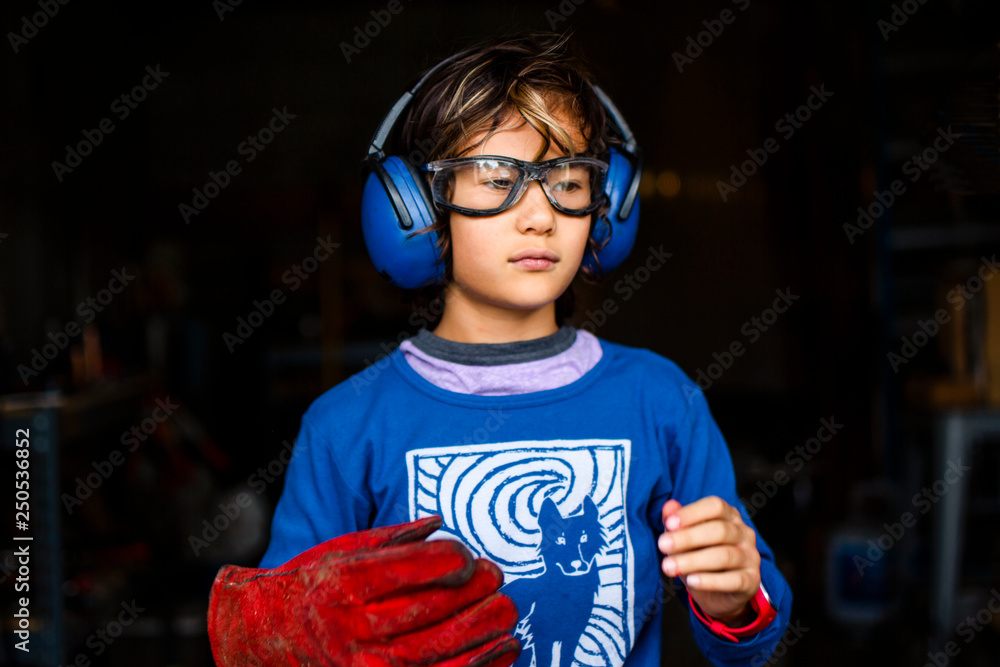 Boy wearing earmuff and safety glasses standing in blacksmith