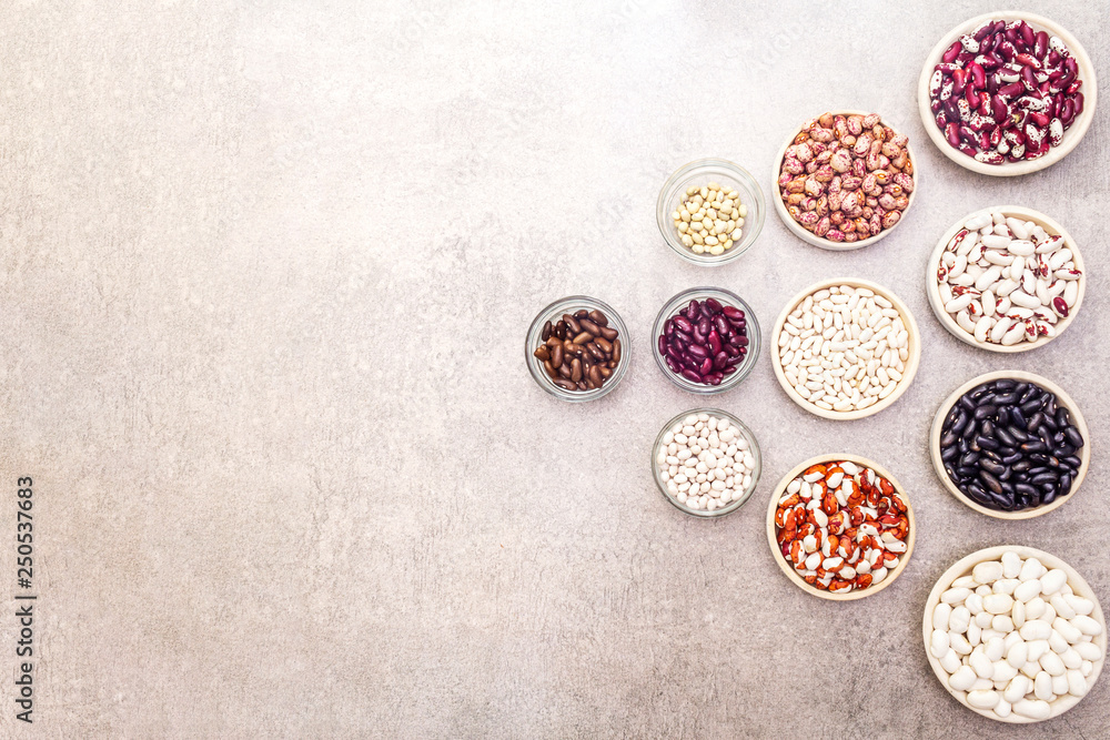 Assortment of beans on a stone background. Crimson cranberry, red, painted pony, black turtle, brown, black-eyed, Jacob's Cattle (heirloom), lima, navy, asparagus bean and soybean. Top view