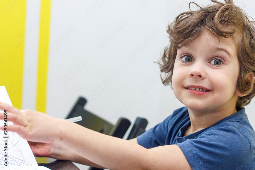 Happy curly boy smiles and sits at a table Happy curly boy smiles and sits at a table