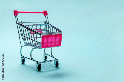 Sale buy mall market shop consumer concept. Small supermarket grocery push cart for shopping toy with wheels isolated on blue pastel colorful paper trendy background. Copy space