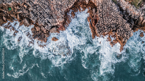 Fotografía Drone aerial top view of sea waves hitting rocks on the beach with turquoise sea water
