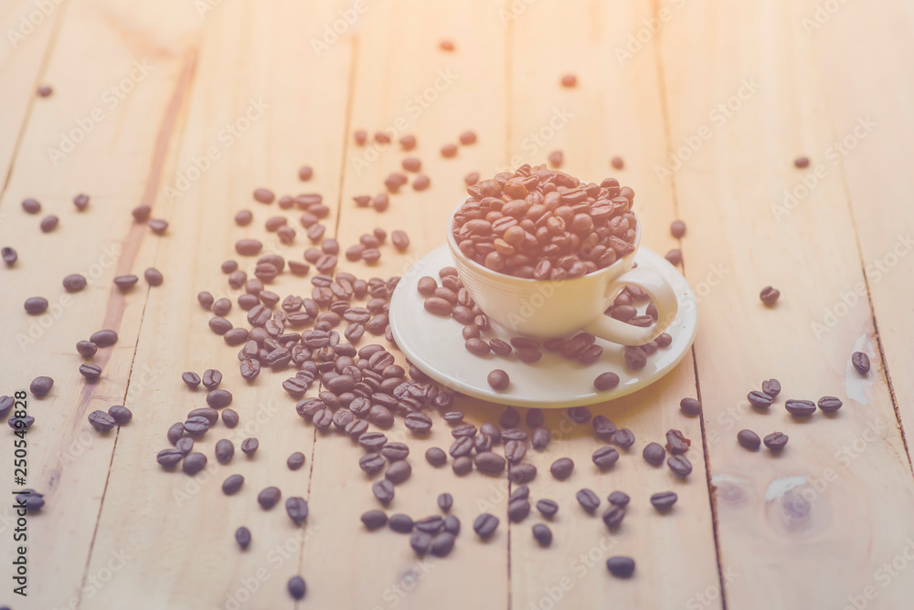 White cup full of coffee beans on Roasted Coffee Beans and wood background, top view White cup full of coffee beans on Roasted Coffee Beans and wood background, top view