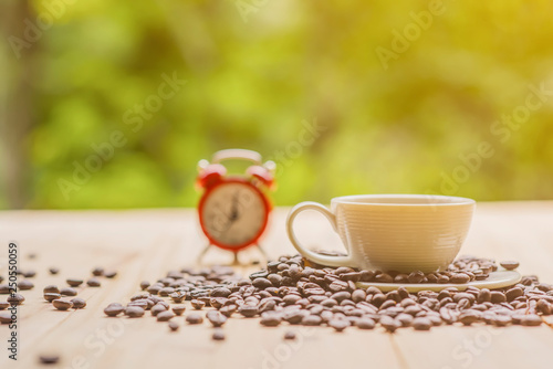 White coffee cup with red alarm clock with nature background