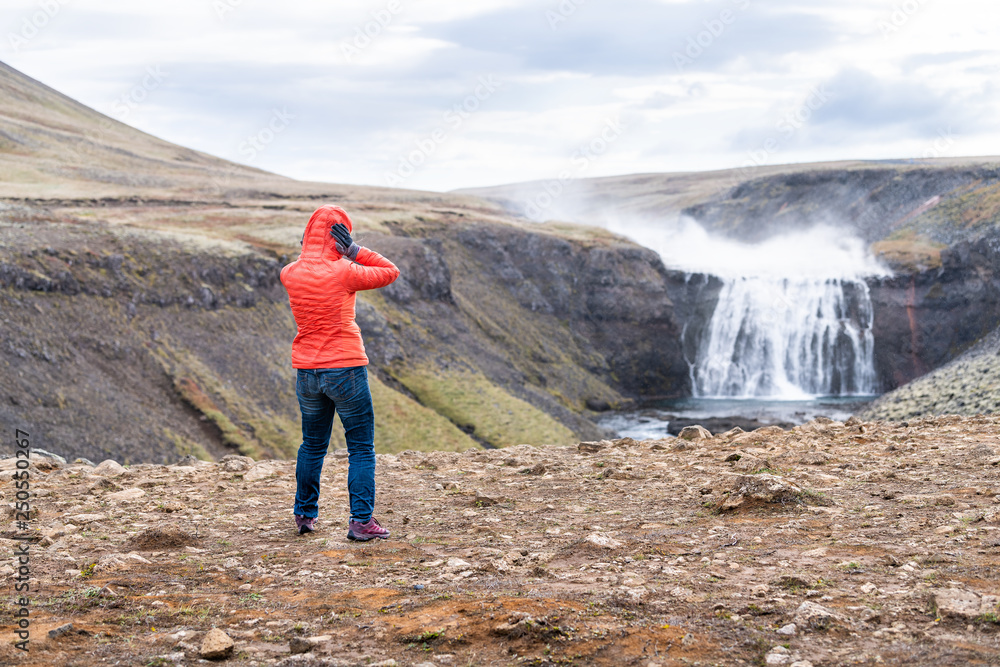 Thorufoss waterfall windy landscape on Golden Circle in Iceland with water flowing on rocks river from cliff and woman tourist in jacket holding head