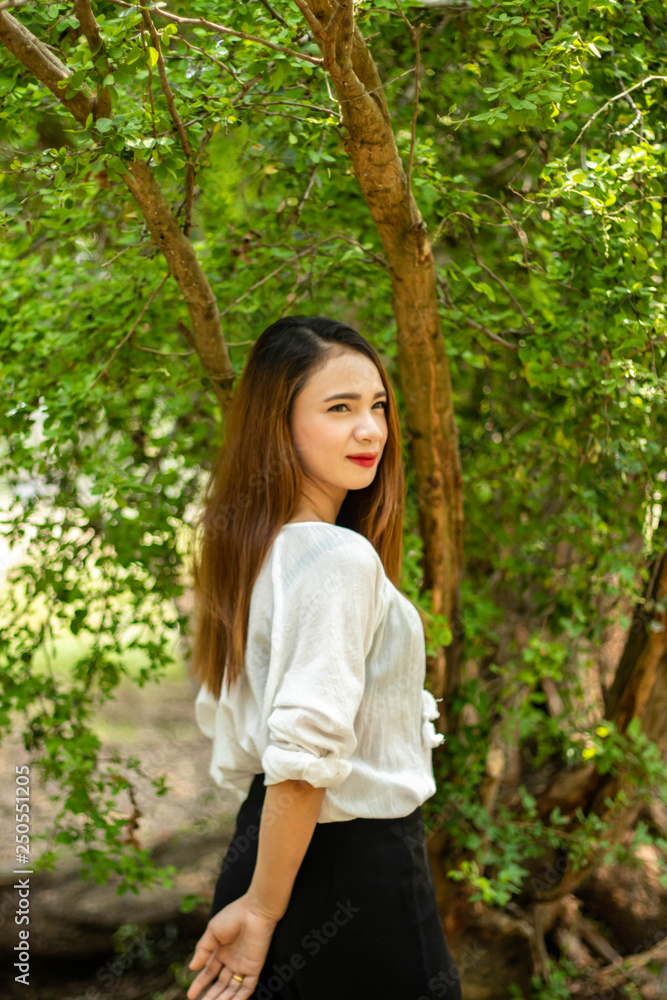 Women white skin lovely brown hair red lip wear white shirt women standing poses photography portrait In the garden has a tree as a background. Women white skin lovely brown hair red lip wear white shirt women standing poses photography portrait In the garden has a tree as a background.