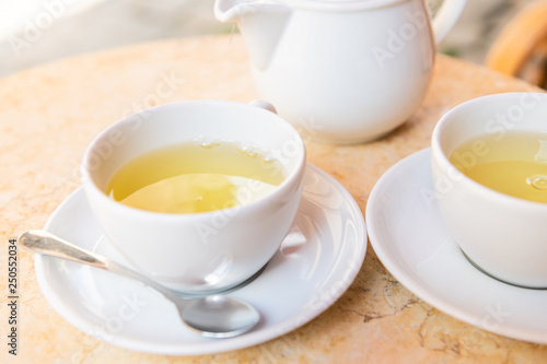 Closeup of two white cups on plates saucers of green or oolong tea in breakfast brunch outdoor cafe restaurant outside table with teapot pot