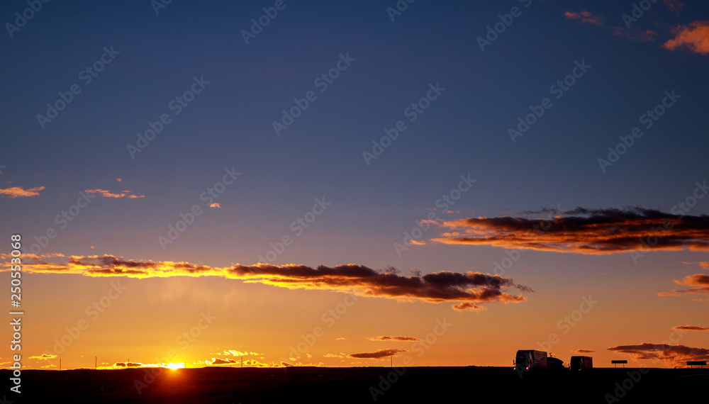 Fototapeta premium Truck cars on a highway at sunrise with beautiful sun in background