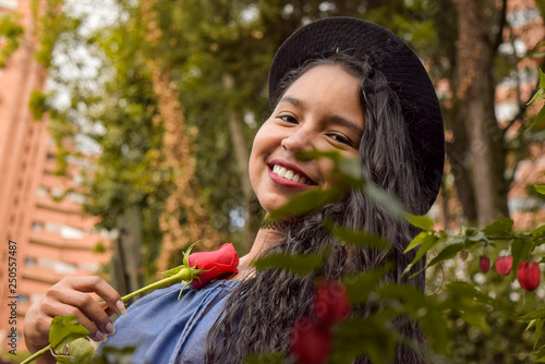 A young brunette in love burns with passion while holding a beautiful red rose. She shows off her wide smile in conjunction with her blue dress and her fedora hat. photo