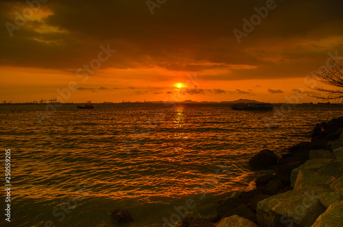 image of a boat floating on the sea with a large sun at sunset © Kittipat