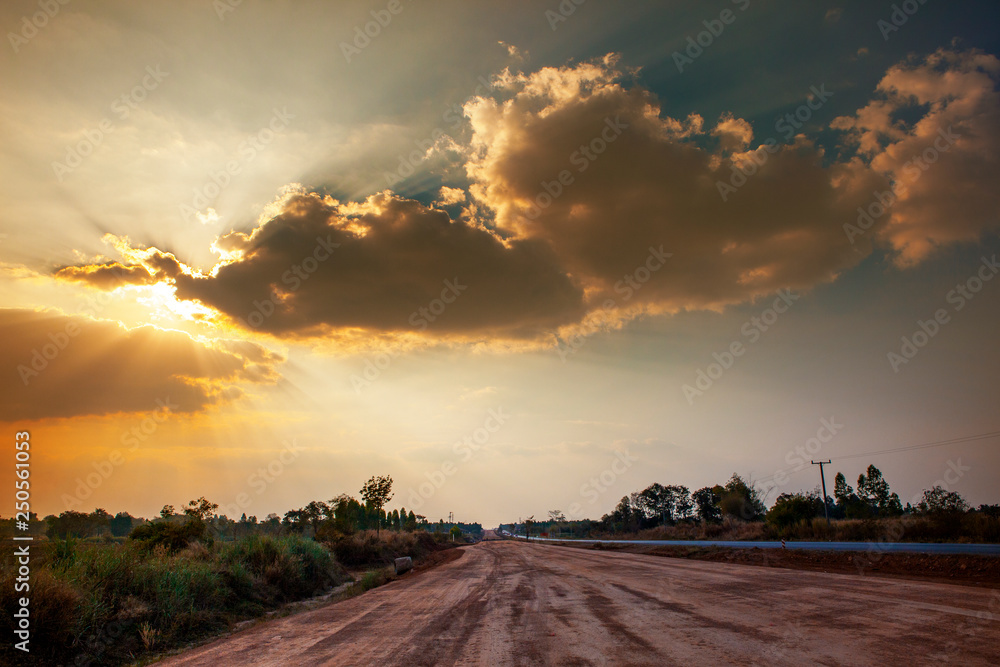 country road and beautiful sun light over dramatic sky