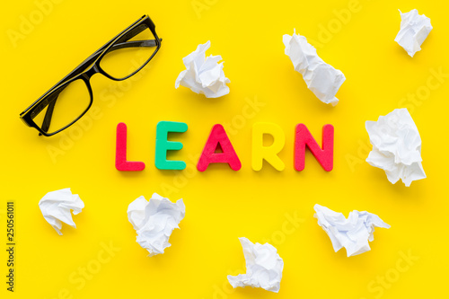 Learn concept. Word learn lined with colorful letters near crumpled paper on yellow background top view