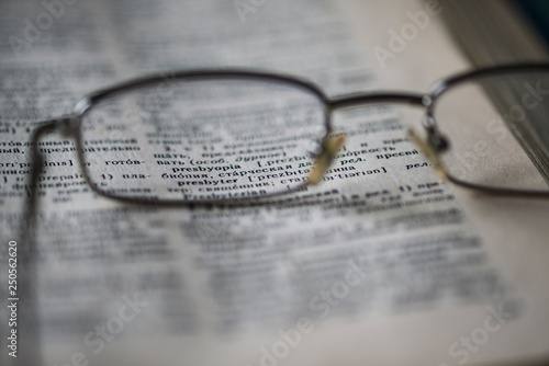 Points are on the page of the English-Russian dictionary. The word  presbyopia can be seen through the glasses lens. Concept  glasses help with vision problems. Selective focus. Blurred image.