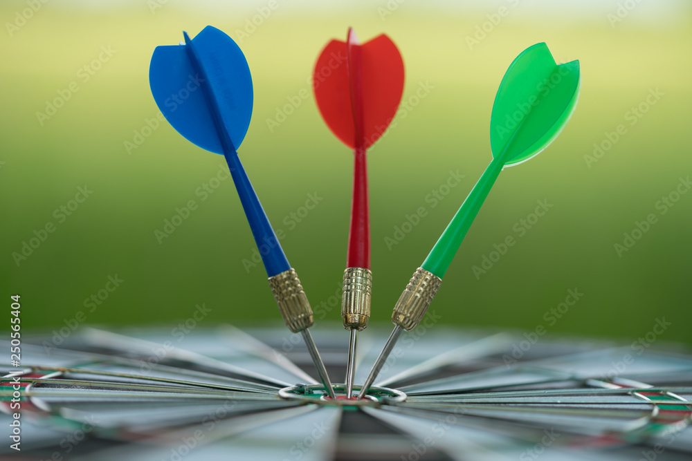 Three dart arrows hitting in the target center of dartboard with green nature background. Target business, achieve and victory concept. Three dart arrows hitting in the target center of dartboard with green nature background. Target business, achieve and victory concept.