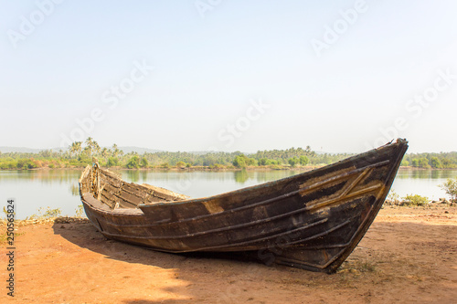 old broken boat on the shore against the backdrop of the river and the green jungle.