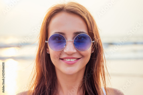 Close up shot of good looking female tourist enjoys free time outdoor near ocean beach, looks at camera during leisure on sunny summer day making selfie. Happy smiling tourist in tropics air kiss © yurakrasil