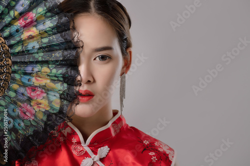 Portrait Of Asian At Traditional Chinese Dress. Close up fashion shot of asian woman holding Chinese fan look at camera on grey background free from copy space. Chinese new year concept