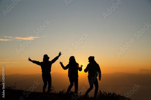 Silhouette of young woman are standing on top of the mountain with raised hands relaxing with sunrise by nature at sunrise, Life style, Group of happy at sunrise or sunset, First morning light