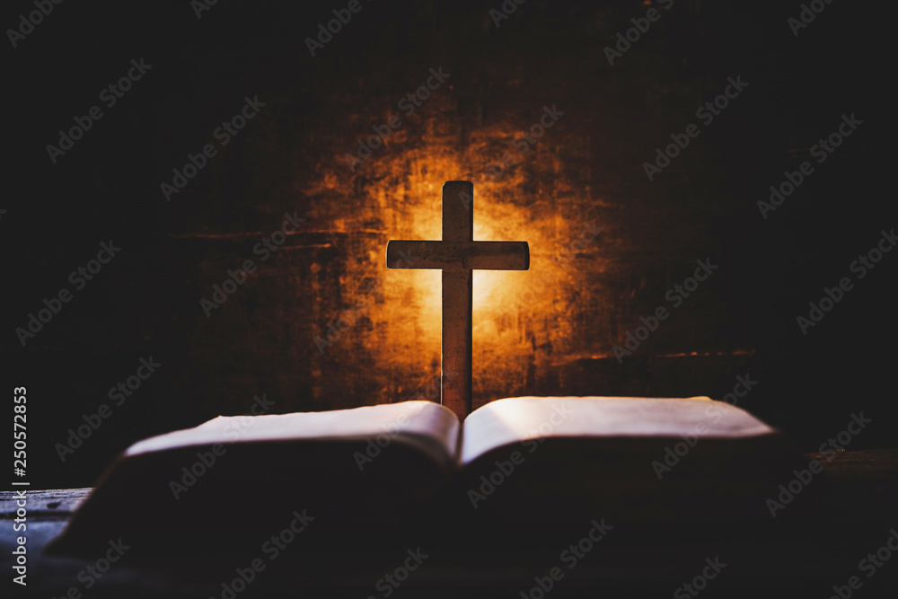 Cross with bible and candle on a old oak wooden table. Beautiful gold background. Religion concept.