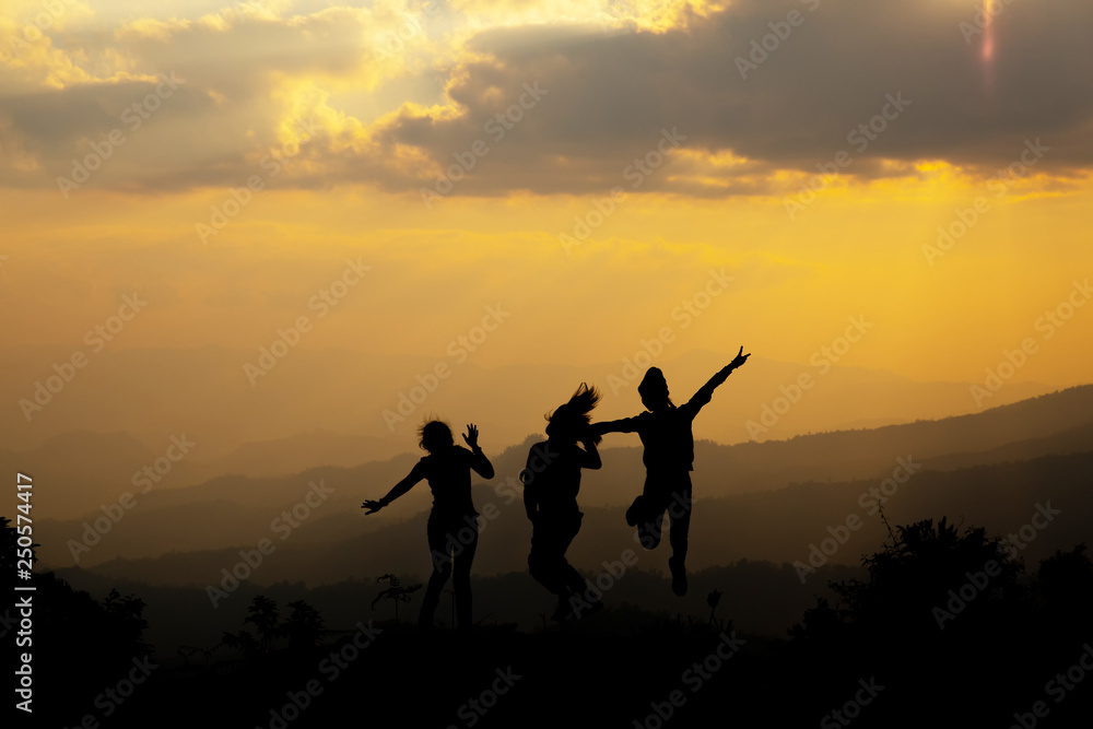 Group of happy people jumping in the mountain at sunset, concept about having fun on the hill, silhouette