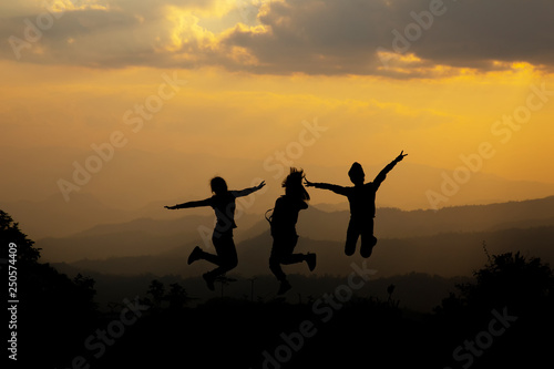 Group of happy people jumping in the mountain at sunset, concept about having fun on the hill, silhouette