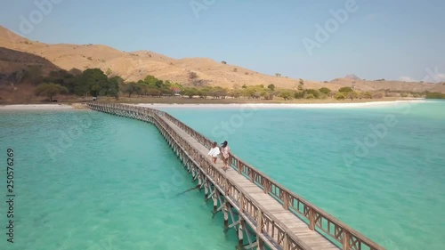 Wallpaper Mural aerial shot of a wooden bridge linking the two shores, crossing blue waters of the gulf, two young women in beach cover-ups are running across the bridge Torontodigital.ca