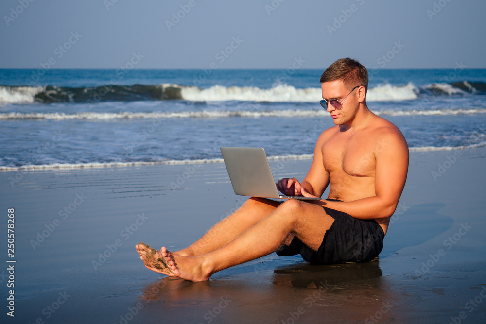handsome and successful man in a stylish well-dressed freelancer working laptop meditating in the lotus position on the beach.freelance and remote work.businessman namaste and om ocean