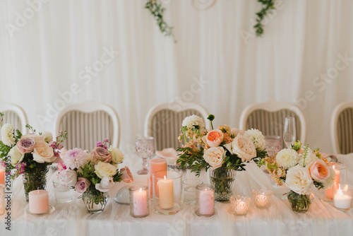 Coziness and style. Modern event design. Table setting at wedding reception. Floral compositions with beautiful flowers and greenery, candles, laying and plates on decorated table.