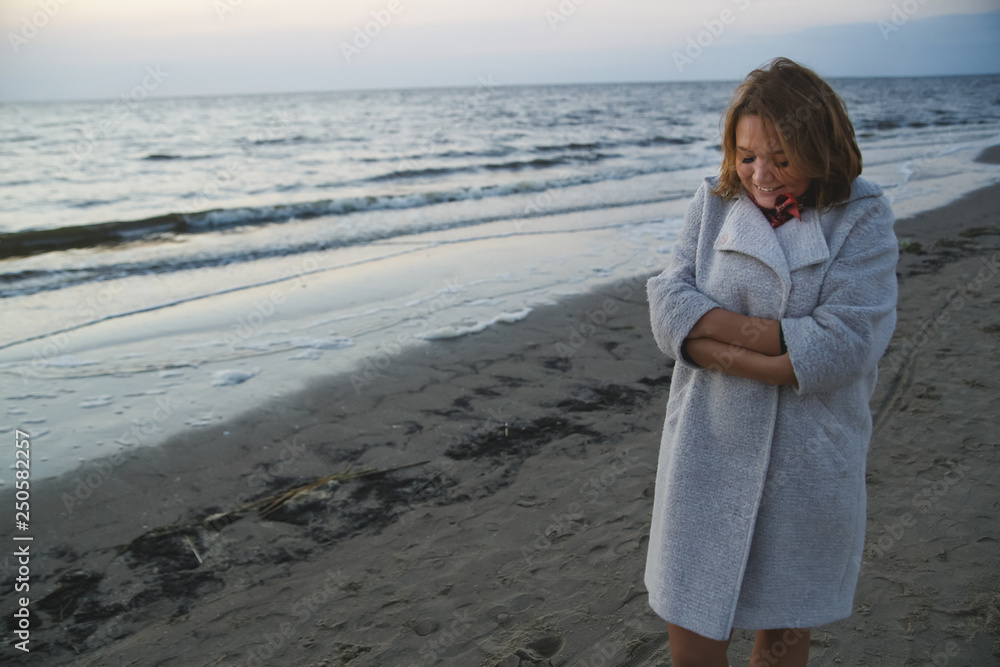 Happy girl walks in a coat along the seashore in the evening. Happy girl walks in a coat along the seashore in the evening.