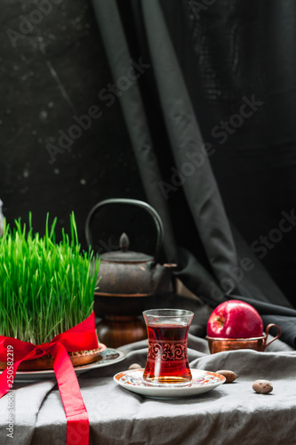 Novruz setting in Azerbaijan with black tea in armudu pear shape drinking glass with green wheat grass semeni with red ribbon for celebration. Spring equinox, Persian Nowruz greeting card copy space 