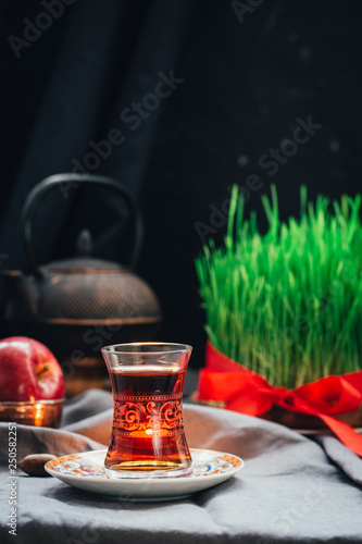 Novruz setting in Azerbaijan with black tea in armudu pear shape drinking glass with green wheat grass semeni with red ribbon for celebration. Spring equinox, Persian Nowruz greeting card copy space  photo