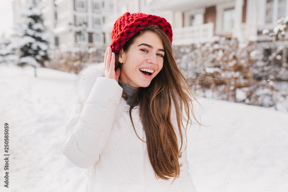 Happy sunny frozen morning on winter time of joyful young woman in red hat, with long brunette hair having fun on street full with snow. Waiting for christmas, new year mood, winter holidays Happy sunny frozen morning on winter time of joyful young woman in red hat, with long brunette hair having fun on street full with snow. Waiting for christmas, new year mood, winter holidays