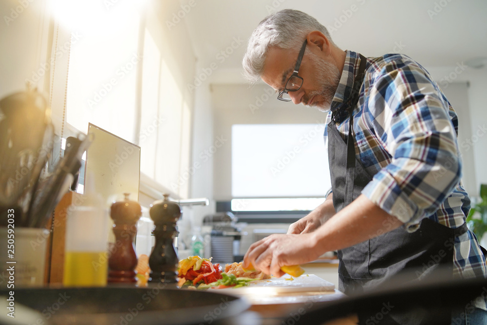 Cheerful mature man in kitchen preparing dish