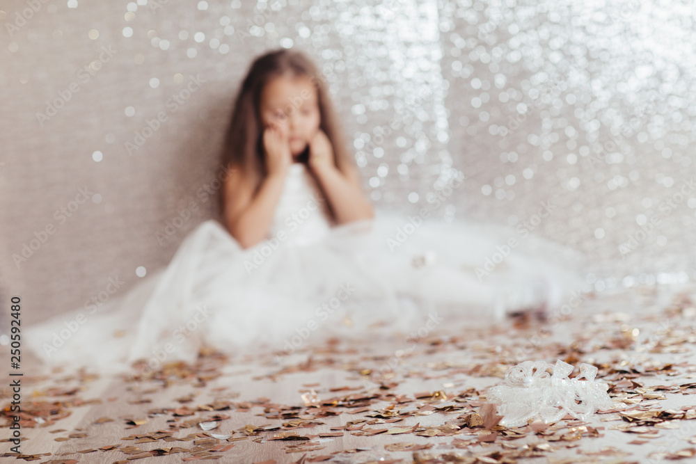 blur sad little child girl in dress sitting on the floor with confetti on  background with silver bokeh. focus on the crown in the foreground Stock  Photo | Adobe Stock