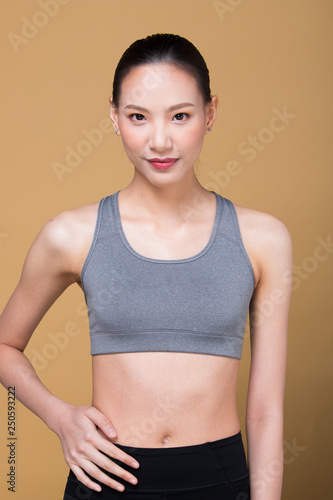 Asian slim Fitness woman exercise warm up stretch spring jumps legs, studio lighting yellow beige mustard background sun shadow copy space, concept Woman Can Do athlete Sport 6 packs