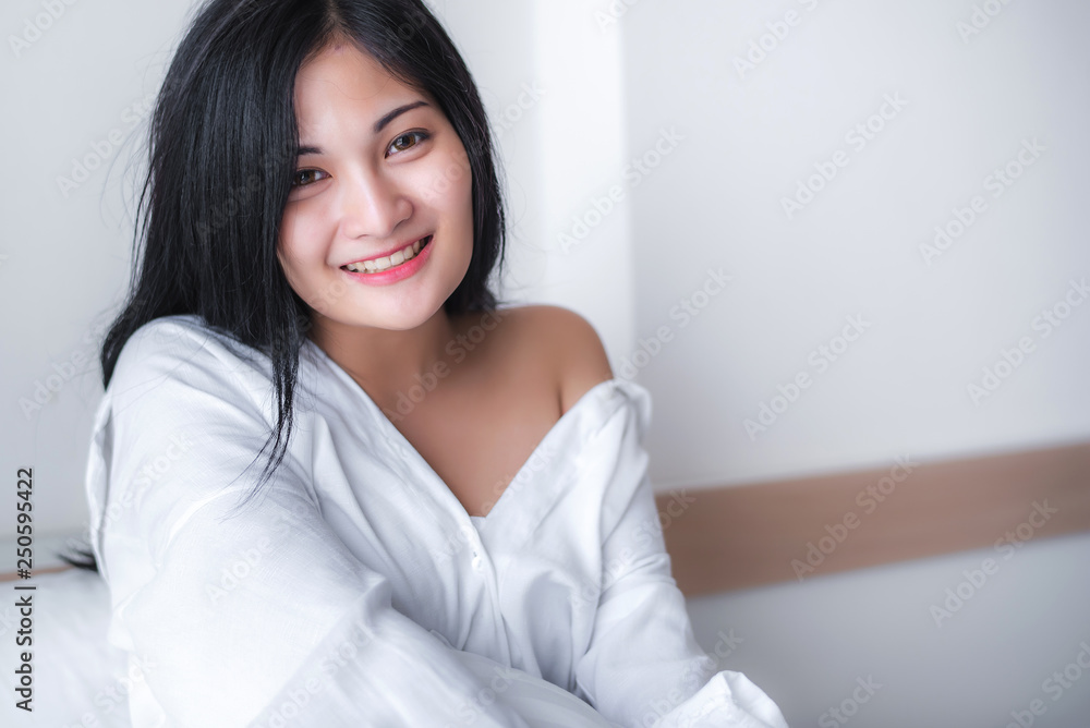 Beautiful young pretty Asian woman wake up and make happy smile with white shirt at the white bed in the morning. Beautiful young pretty Asian woman wake up and make happy smile with white shirt at the white bed in the morning.