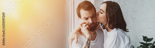 beautiful woman kissing man talking on smartphone at home with copy space and sunlight