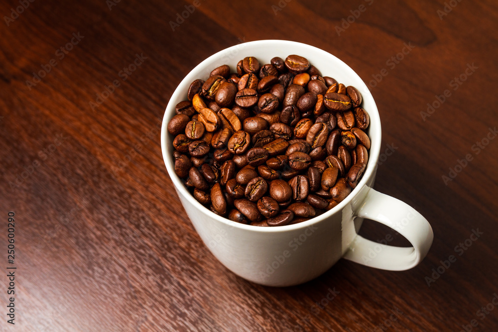 Fototapeta premium Roasted Coffee beans in a white mug cup isolated on a rustic wood table